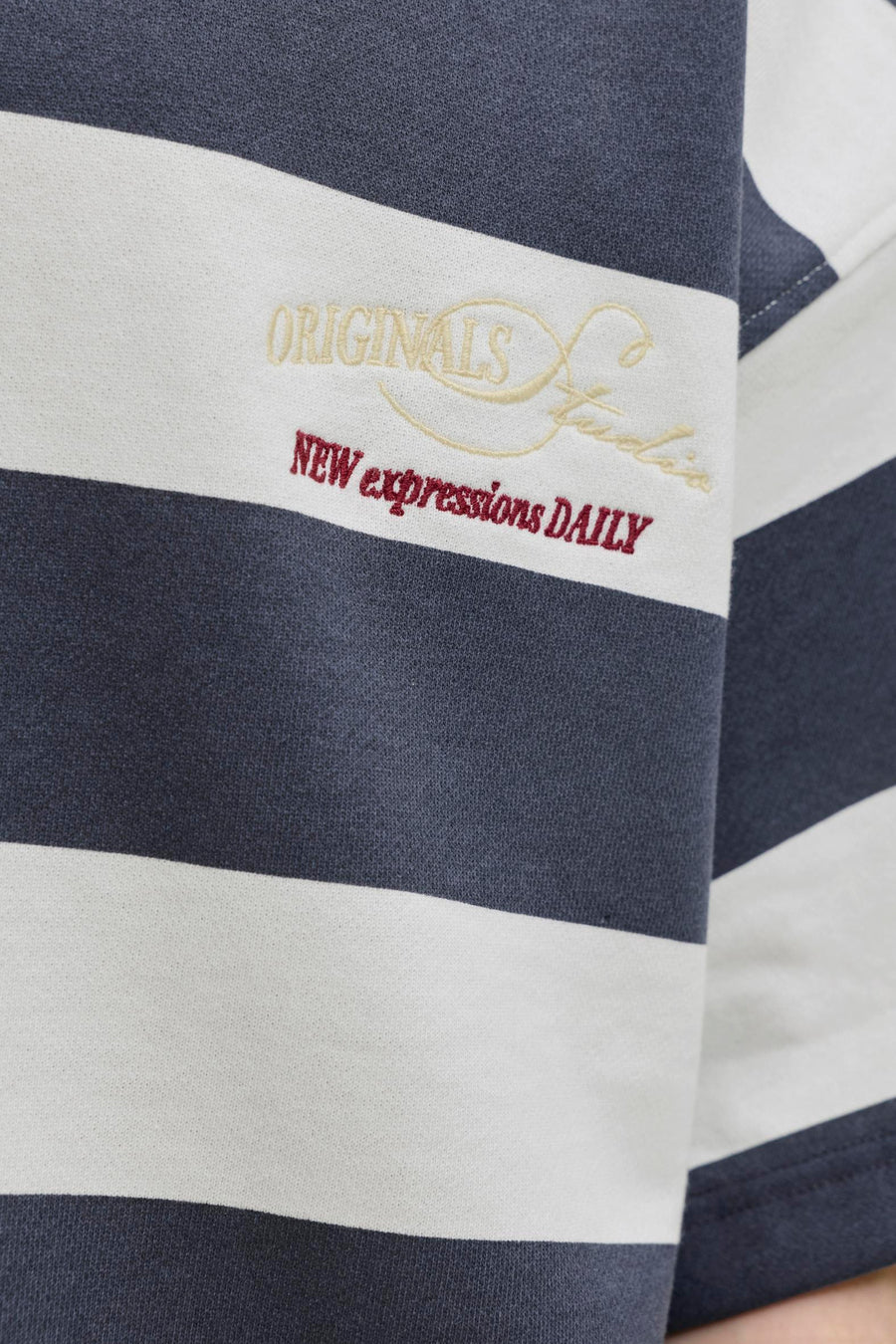 Pull gris rayé à col rond de ORIGINALS BY JACK & JONES, avec inscription brodée crème 'ORIGINALS' et texte brun-rouge 'NEW expressions DAILY'.