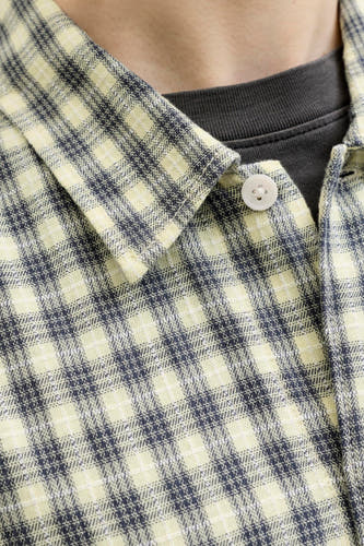 Multicolor geruit overhemd van ORIGINALS BY JACK & JONES, close-up van kraag en knoop, lichte stof met donkerblauwe en crèmekleurige ruitjes, gedragen over een donkergrijze trui