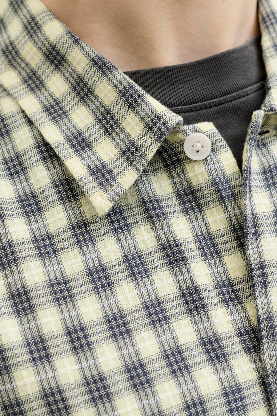Multicolor geruit overhemd van ORIGINALS BY JACK & JONES, close-up van kraag en knoop, lichte stof met donkerblauwe en crèmekleurige ruitjes, gedragen over een donkergrijze trui