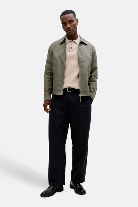 Beige geribbelde poloshirt van PREMIUM by JACK & JONES, gedragen onder een open groen jasje met zwarte broek en lakschoenen.