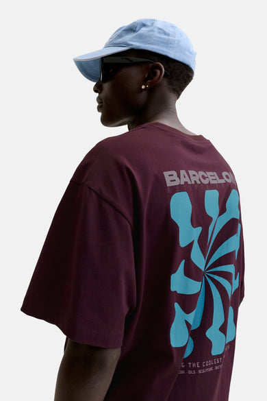 Paarse korte mouwen t-shirt van ORIGINALS BY JACK & JONES, met grote blauwe grafische print op rug, zijaanzicht model met pet en zonnebril