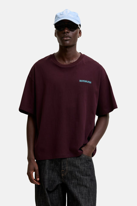Paarse korte mouw T-shirt van ORIGINALS BY JACK & JONES met klein logo op borst, gedragen in lifestyle shot met donkere jeans en pet