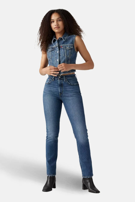 Vrouw in jeans en denim vest, staand.