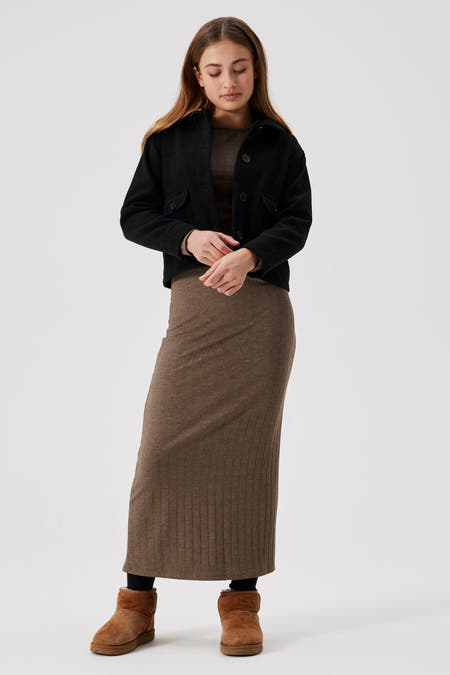 Manteau court en denim noir de LMTD, avec fermeture à boutons et poches brodées, porté sur une jupe brune.