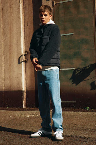 Manteau court noir de LMTD, porté avec un T-shirt blanc, des jeans et des baskets.