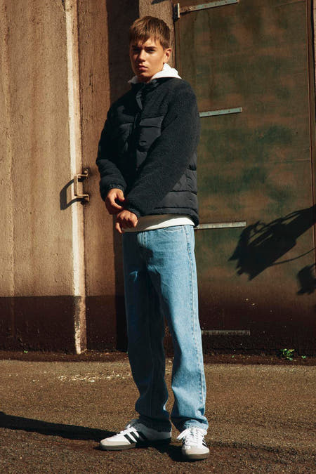 Manteau court noir de LMTD, porté avec un T-shirt blanc, des jeans et des baskets.