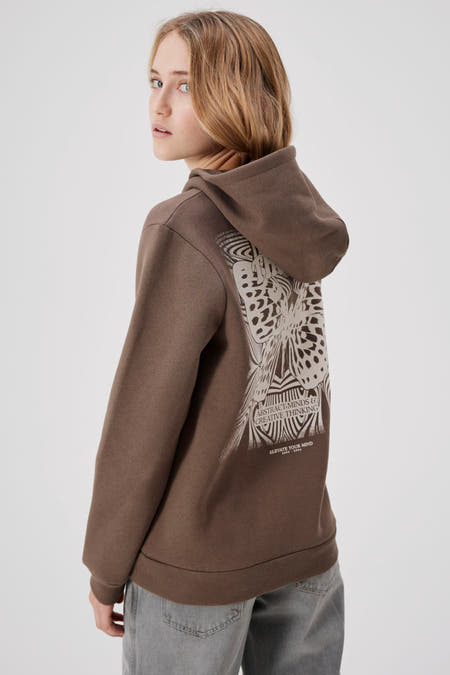 Pull-over marron avec capuche LMTD, imprimé de papillon et associé à des jeans gris et des baskets blanches.