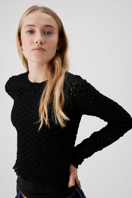 Pull noir de LMTD, avec des manches longues et un motif texturé, associé à un pantalon en denim.