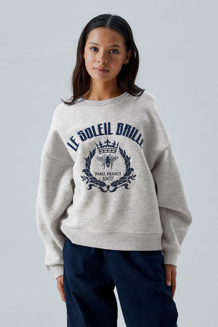 Pull-over gris de LMTD avec imprimé bleu marine sur l'avant, associé à des pantalons bleu marine et des baskets grises.