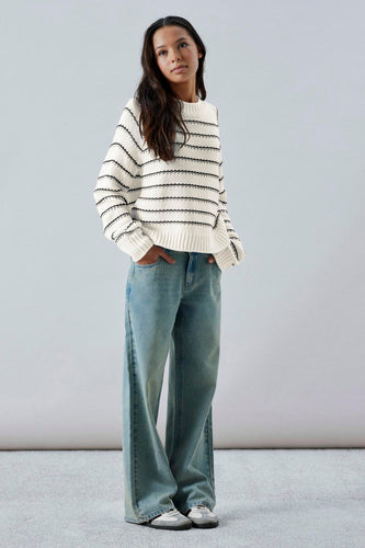Vrouw met gestreepte trui en wijde jeans.
