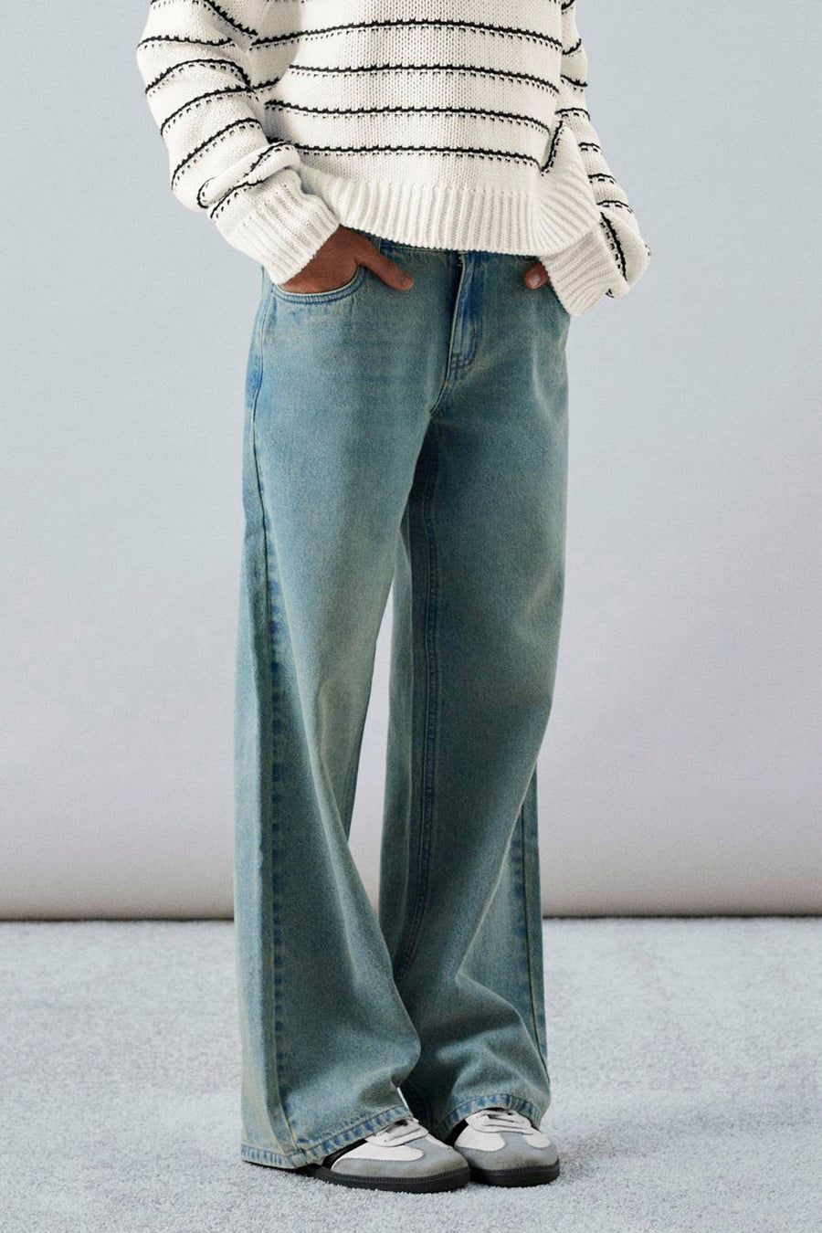 Persoon met gestreepte trui en wijde jeans staat met handen in de zakken.