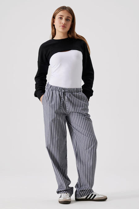 Jean noir de LMTD, associé à une chemise blanche et un pantalon rayé gris, avec des fermetures éclair et des baskets.