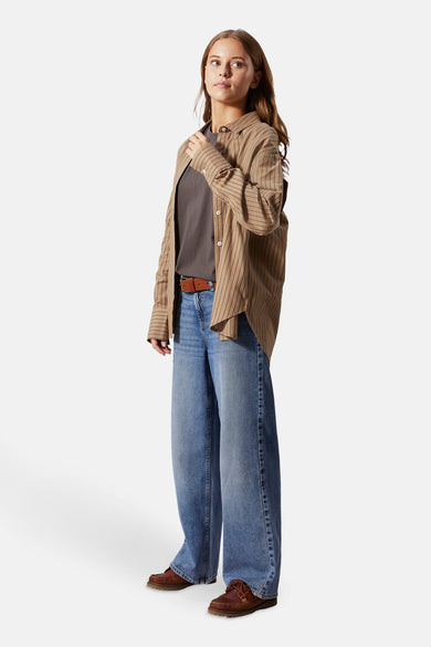 Jean bleu, large de LMTD, porté avec un ceinture marron, chemise rayée marron et mocassins marrons.