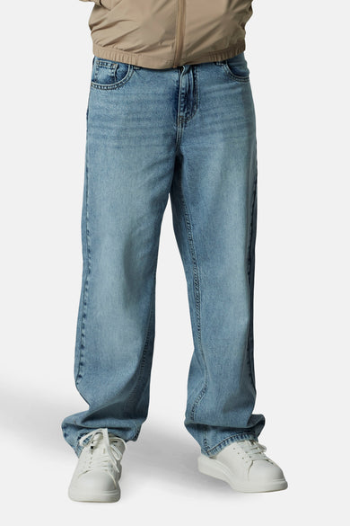 Jean en denim bleu clair large de LMTD, avec des baskets blanches et un manteau beige.