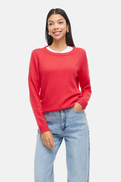 Pull-over rouge avec col rond de VILA®, porté avec un T-shirt blanc et des jeans bleus, et des chaussures noires.