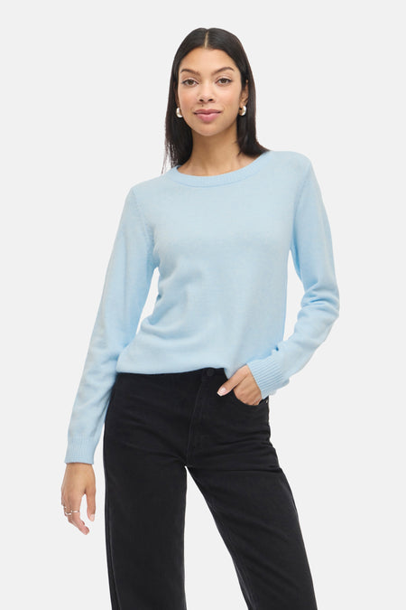 Vrouw met lichtblauwe trui en zwarte jeans.