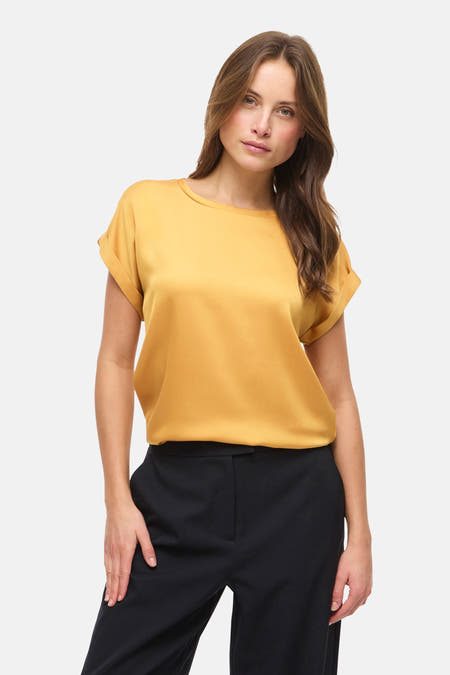 Gouden top met korte mouwen van VILA, gecombineerd met een zwarte pantalon.
