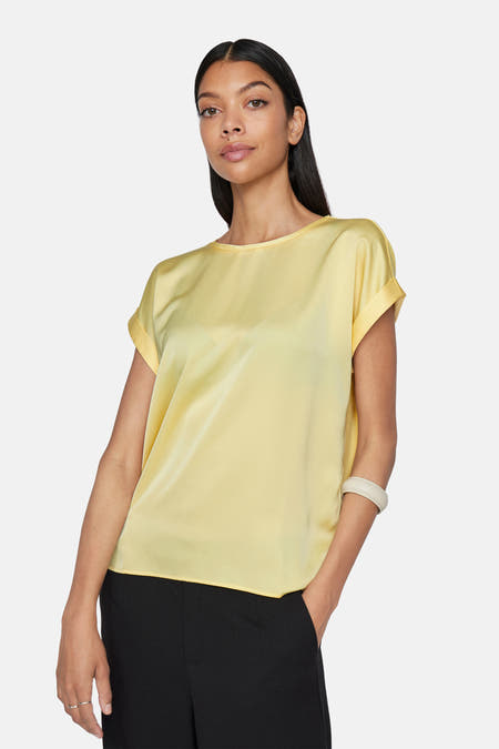 T-shirt jaune à manches courtes de VILA, avec des manches retroussées et associé à un pantalon noir.
