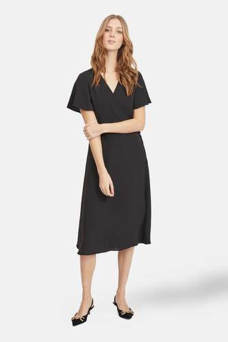 Robe noire à manches courtes de VILA, avec un modèle wrap et portée avec des escarpins noirs à détails dorés.