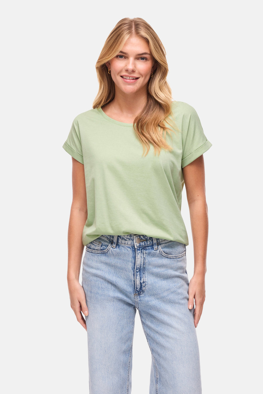 T-shirt vert à manches courtes de VILA®, avec manches retroussées et associé à un jean et des mules blanches.