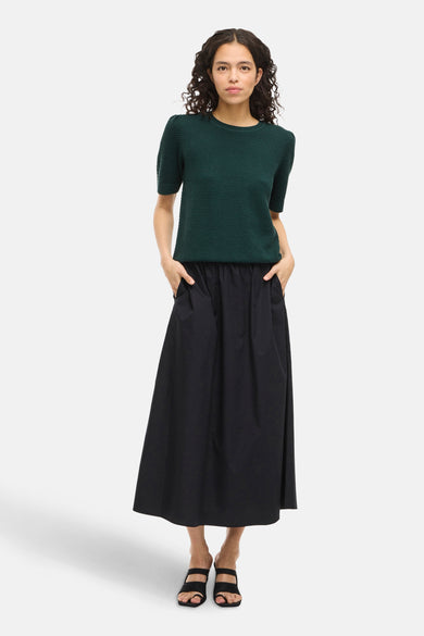 T-shirt vert de VILA, avec des manches courtes, associé à une longue jupe noire et des chaussures ouvertes.