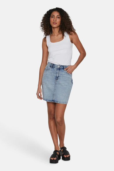 Short skirt of light blue denim from VILA, with a white tank top and black sandals with platform soles.
