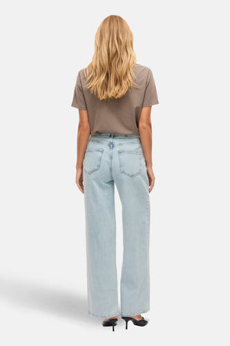Jean bleu clair large de VILA, vu de de derrière, avec un t-shirt marron et des baskets noires.