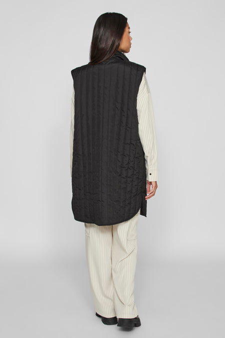 Gilet bodywarmer noir de VILA, avec des coutures verticales, porté sur un chemisier rayé et une jupe.