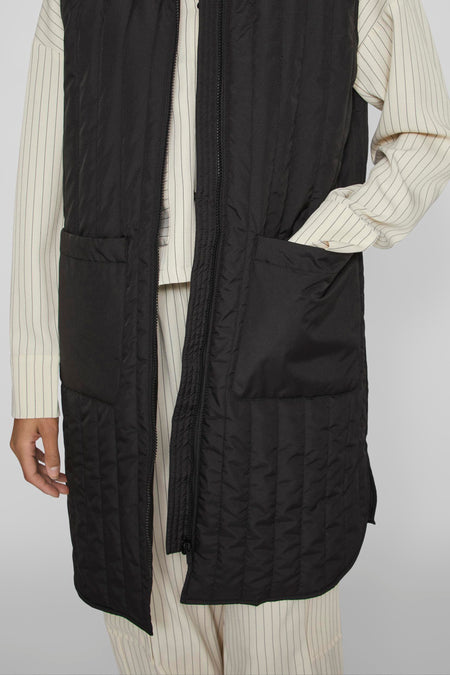 Gilet bodywarmer noir de VILA, avec un motif brodé, des poches et une fermeture éclair, porté sur une tenue rayée.