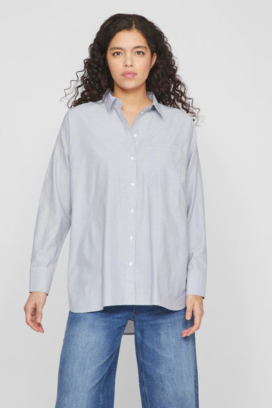 Chemise bleue à rayures horizontales de VILA avec des manches longues, une poche poitrine et portée avec un jeans bleu.
