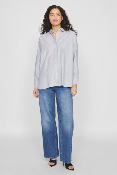 Chemise bleue à manches longues de VILA®, portée avec des jeans larges et des baskets.