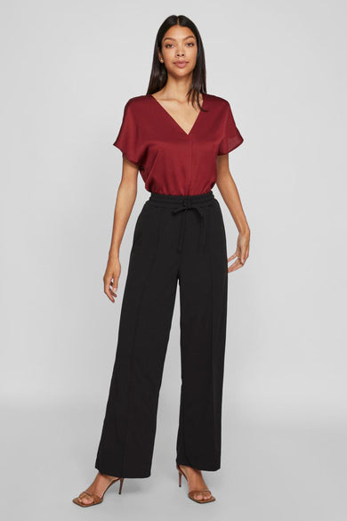 Pantalon noir de VILA®, avec des jambes larges et une ceinture élastiquée, associé à des baskets brunes et un haut bordeaux.