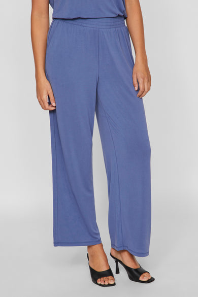 Pantalon bleu de VILA, avec des jambes larges et porté avec des bottines noires à talon.