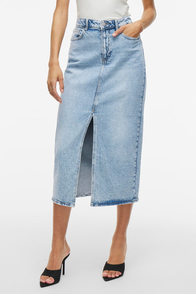 Jupe en denim bleu clair de VILA, avec une fente à l'avant, associée à une chemise blanche et des baskets noires.