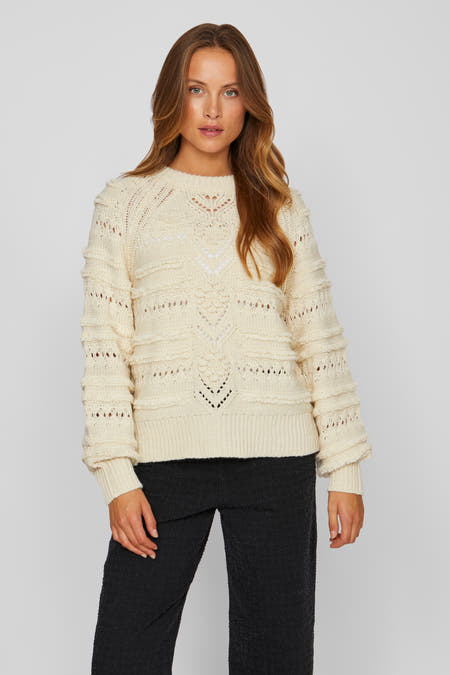 Sweat-shirt écru de VILA, avec un col rond et des détails broés, et des manches longues, porté avec un pantalon noir.
