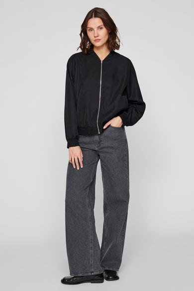 Manteau court noir de VILA®, avec des manches longues et une fermeture éclair argentée, associé à un jean foncé.