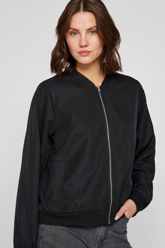 Manteau court noir de VILA avec des manches longues, une fermeture éclair et des poches, porté avec un jean gris.