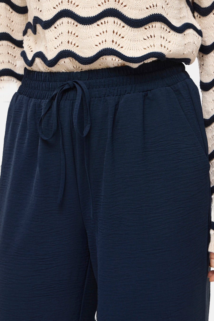 Pantalon bleu de VILA, avec cordon de serrage et texture froissée, combiné avec un pull en maille à motif ondulé.