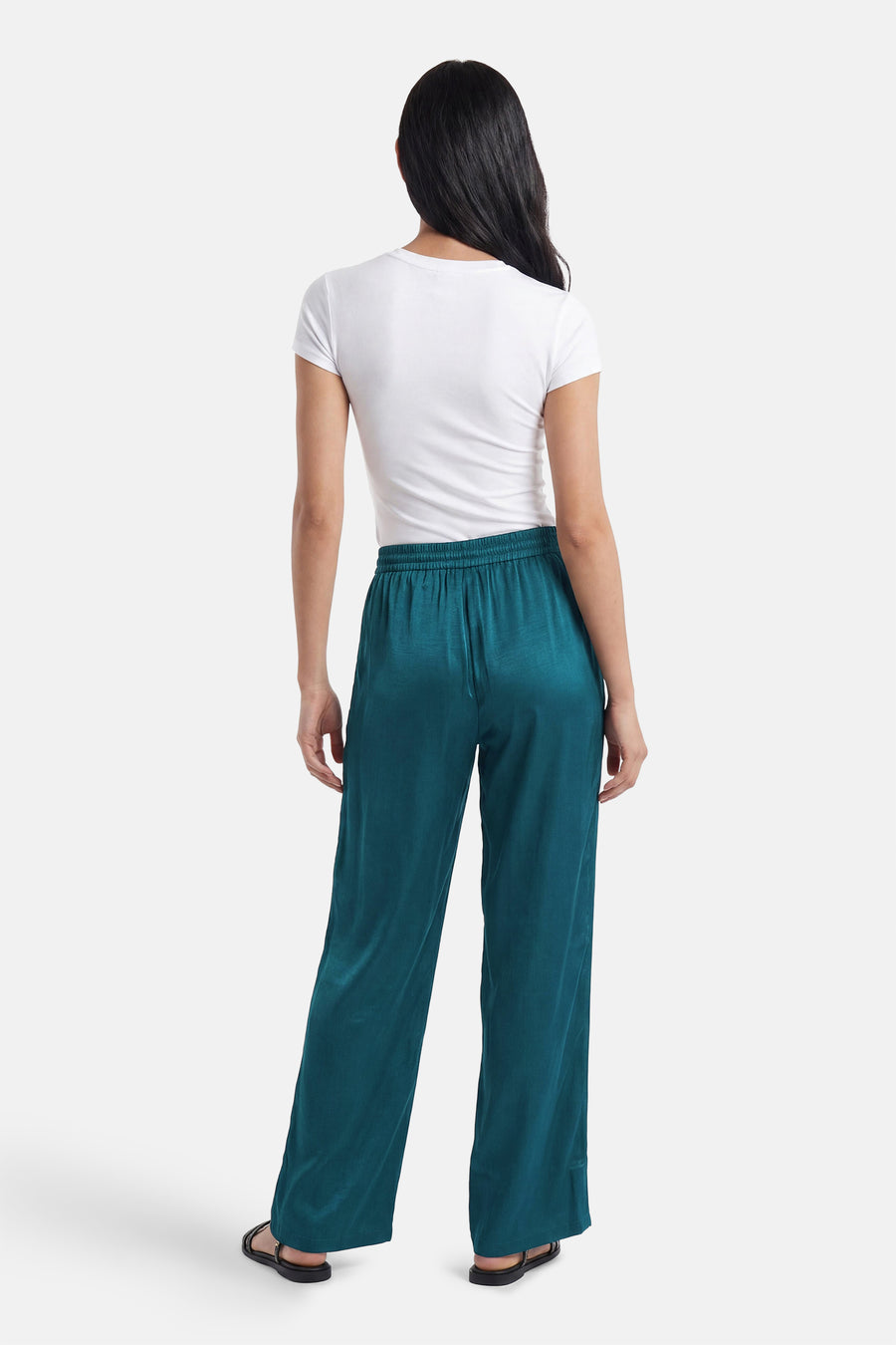 Glanzende petrolgroene broek van VILA® met losvallende pijpen en elastische taille, gedragen met wit t-shirt en zwarte sandalen.