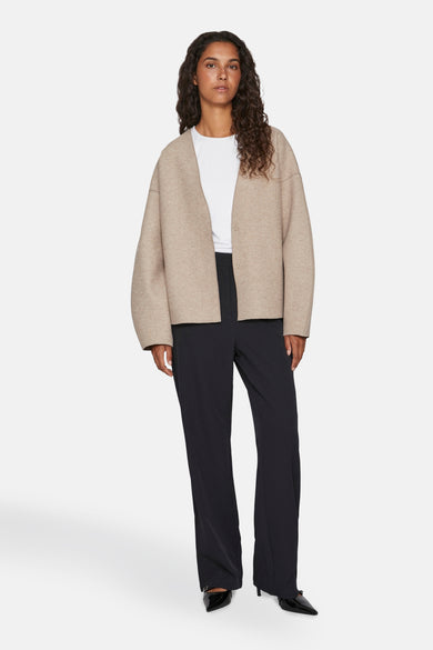 Manteau beige de VILA® avec des manches longues, porté avec un T-shirt blanc et un pantalon noir.