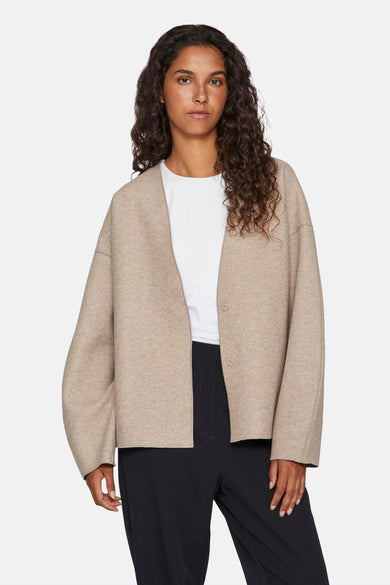 Manteau court beige de VILA, avec des manches longues et une fermeture à boutons, porté sur un chemise blanc et un pantalon noir.