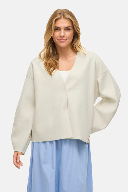 Blouse écru de VILA, portée avec une jupe bleue et des bottes.