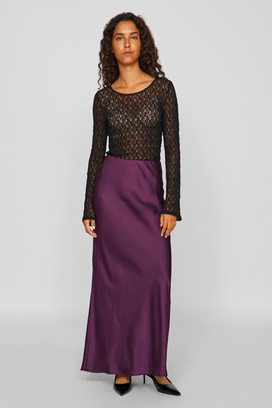 Blouse noire à manches longues de VILA, portée avec une jupe pourpre en soie et des talons noirs.