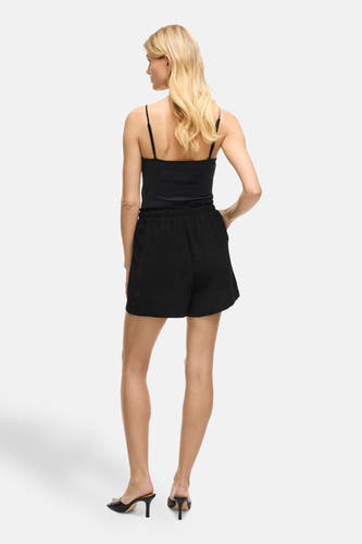 Short noir de VILA, avec une ceinture élastique, porté avec un t-shirt noir et des baskets noires.