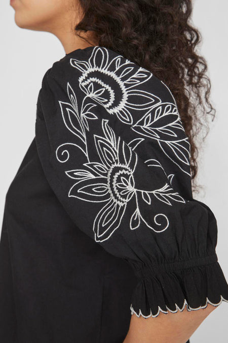 Blouse noire de VILA, avec des motifs floraux brodés sur les manches et un bord plié.