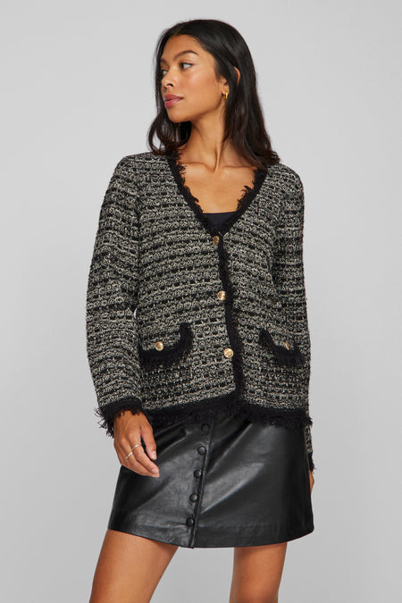 Gilet noir de VILA®, avec fermeture à boutons, poches et bordures froncées, porté avec une jupe en cuir et des chaussettes jusqu'aux genoux.