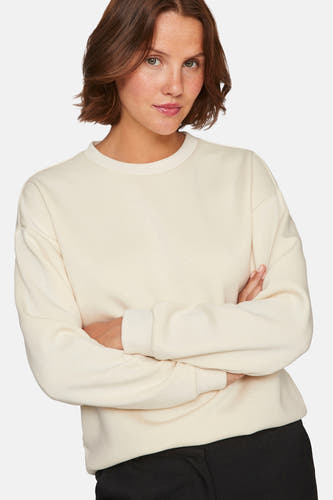 Gilet beige de VILA®, avec des manches longues et des bras croisés, porté avec un pantalon noir.