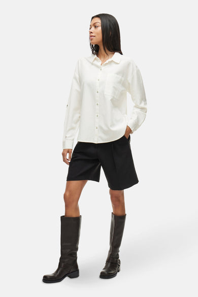 Chemise blanche à manches longues de VILA®, portée avec des short noirs et des bottes hautes.
