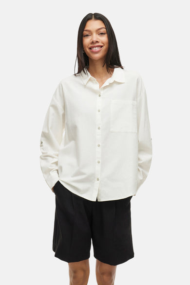 Chemise blanche à manches longues de VILA®, portée avec des short noirs, d'un design simple et d'une poche poitrine.