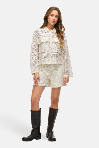 Chemise écru à manches longues de VILA®, avec des détails en dentelle et portée avec des shorts coordonnés et des bottes noires.